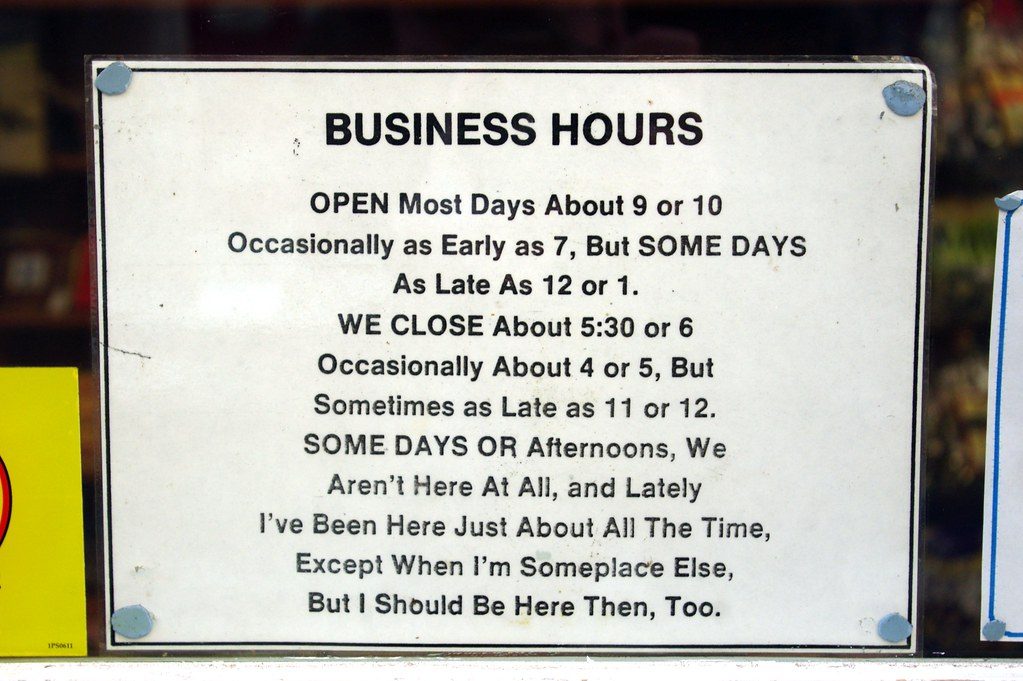 A hand-lettered business hours sign taped in a shop window